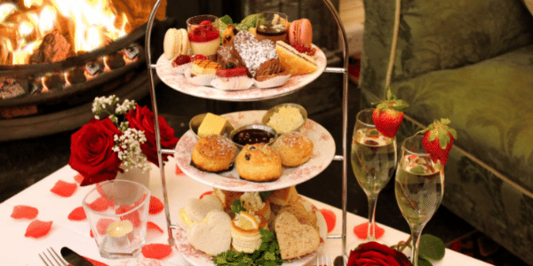 Afternoon Tea with Scones, cakes, sandwiches and vol au vents on white cloth table with roses and fire place 