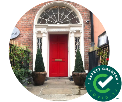 Castle Hotel Entrance with Red door and Georgian fanlight window and red brick and two plants in on the top of the steps. Image is overlaid with Failte Ireland Safety Charter Mark. 