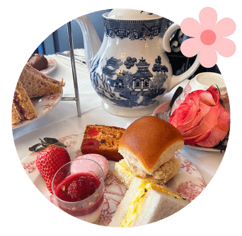 Roses and cakes and sandwiches on a plate with teapot behind