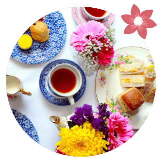 cup of bombay chai organic tea in cup surrounded by sandwiches scones and flowers