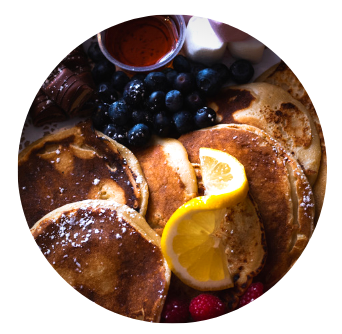 American Style Drop Pancakes with lemon twist, surounded by toppings such as maple syrup in container and kinder bueno pieces, blueberries, marshmallows and raspberries. Copyright Old Music Shop Restaurant 