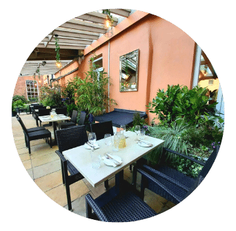 Outdoor Garden Terrace with leafy plants, white tables, black chairs, mirrors and glass roof and Georgian window. Old Music Shop Restaurant at Castle Hotel Dublin 