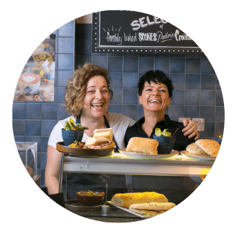Two servers laughing together behind a counter laden with sandwiches at Old Music Shop Restaurant